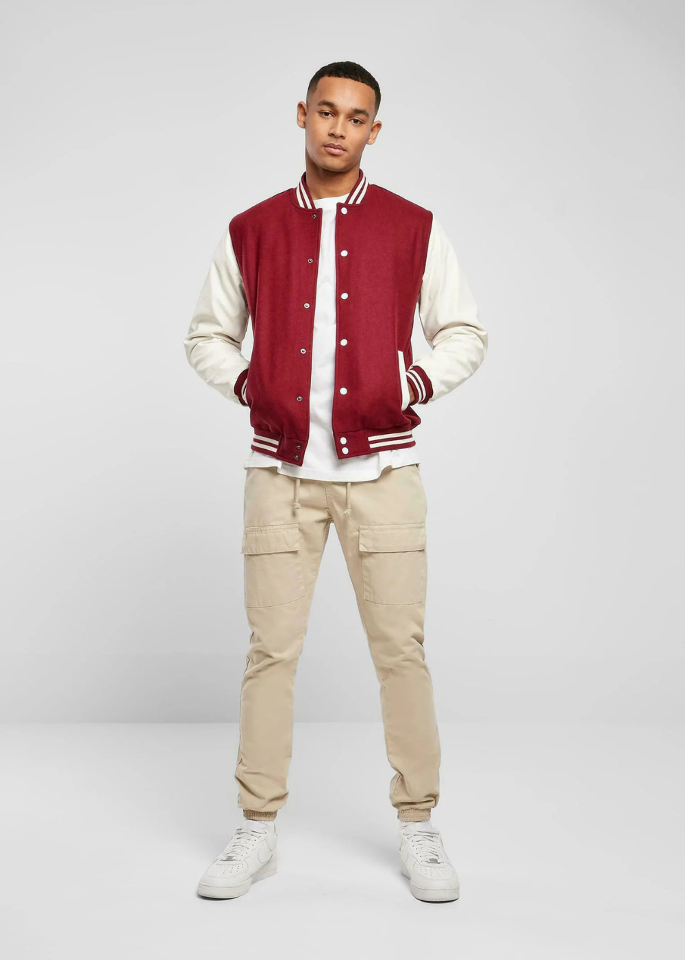 Stylish red and white varsity jacket worn by a young man, paired with beige cargo pants and white sneakers – perfect for a casual, sporty look.